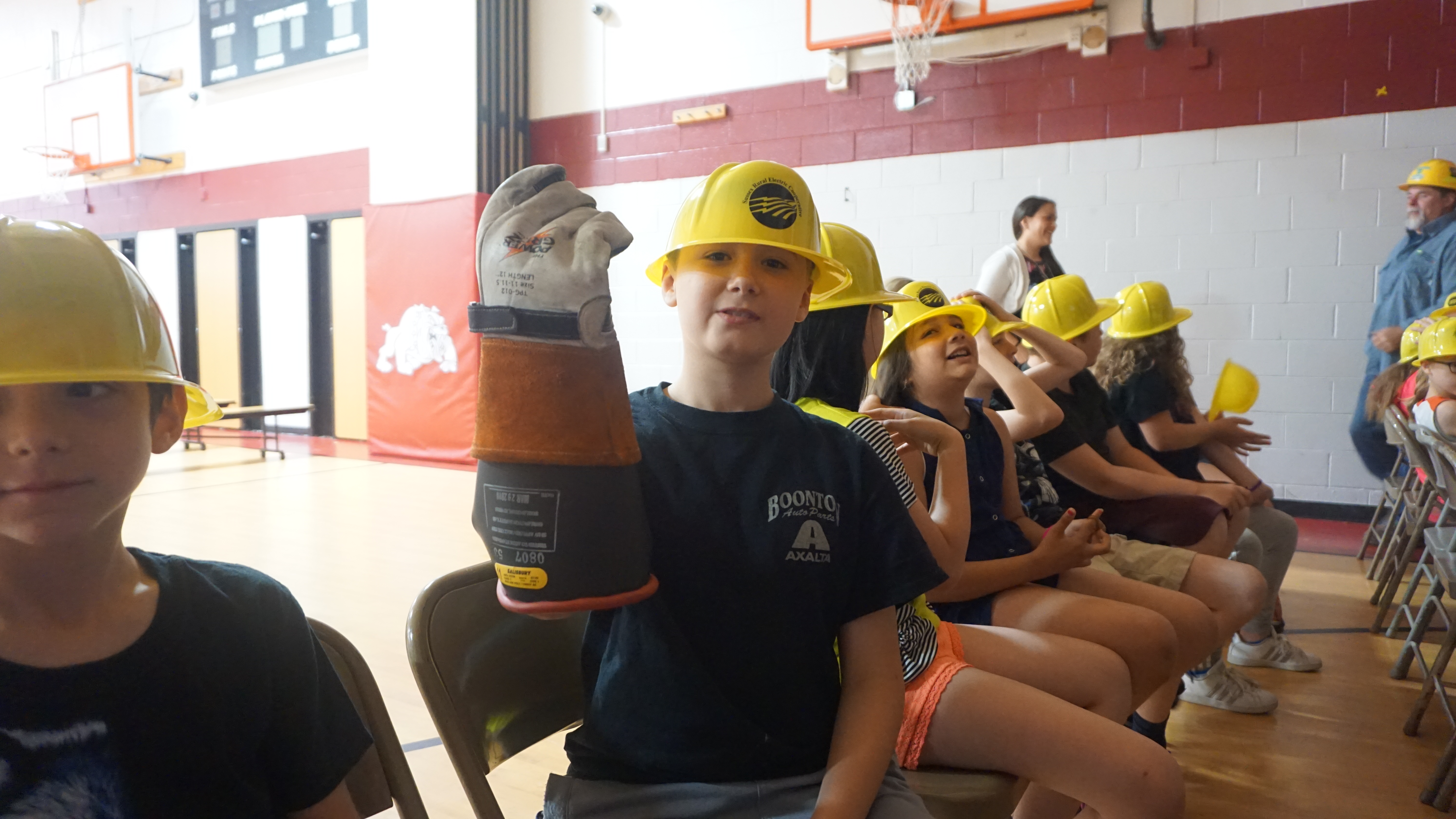 Photo of a fourth grade student holding up a lineman's glove while wearing an SREC plastic hardhat
