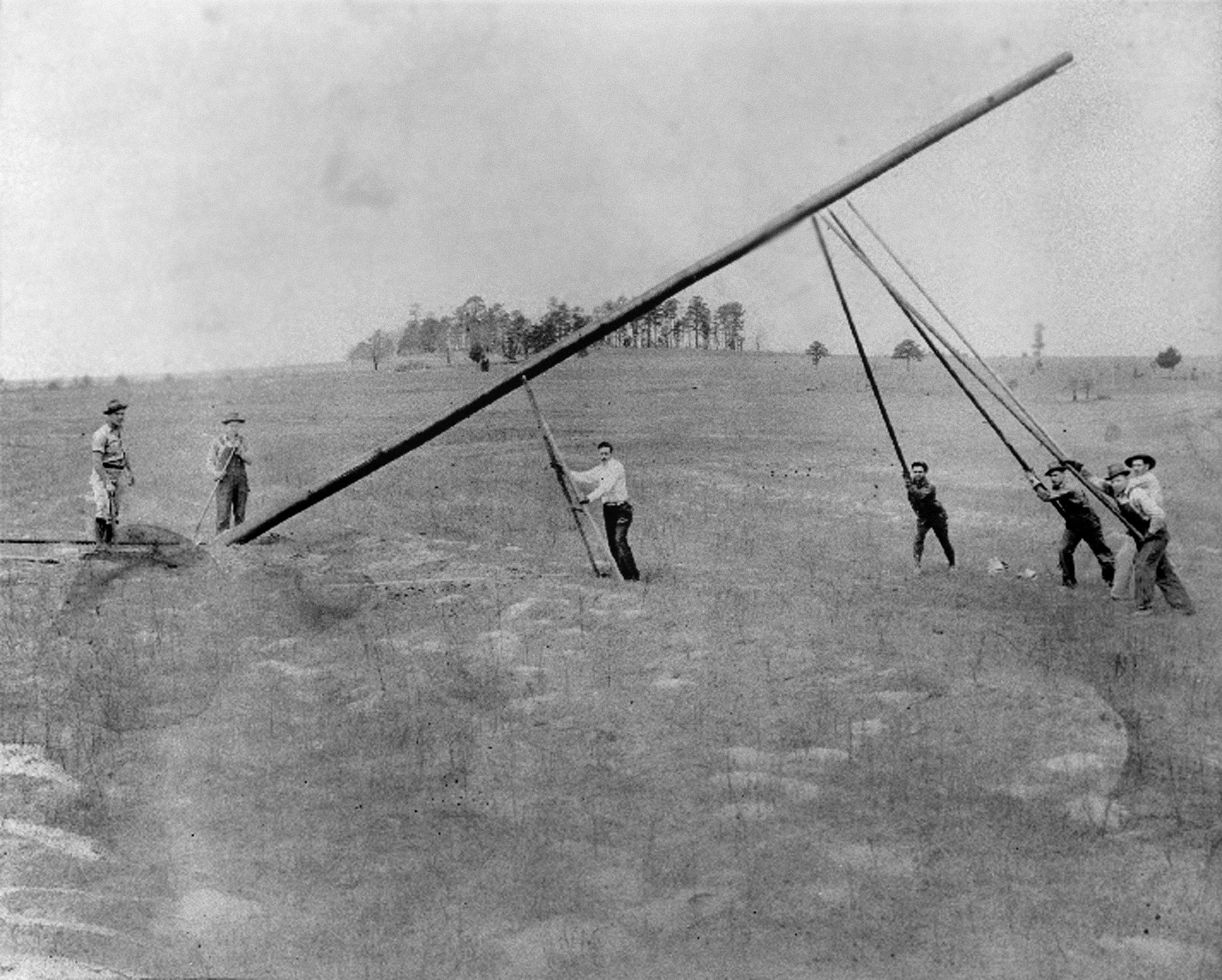 A group of men work together to raise a utility pole by hand