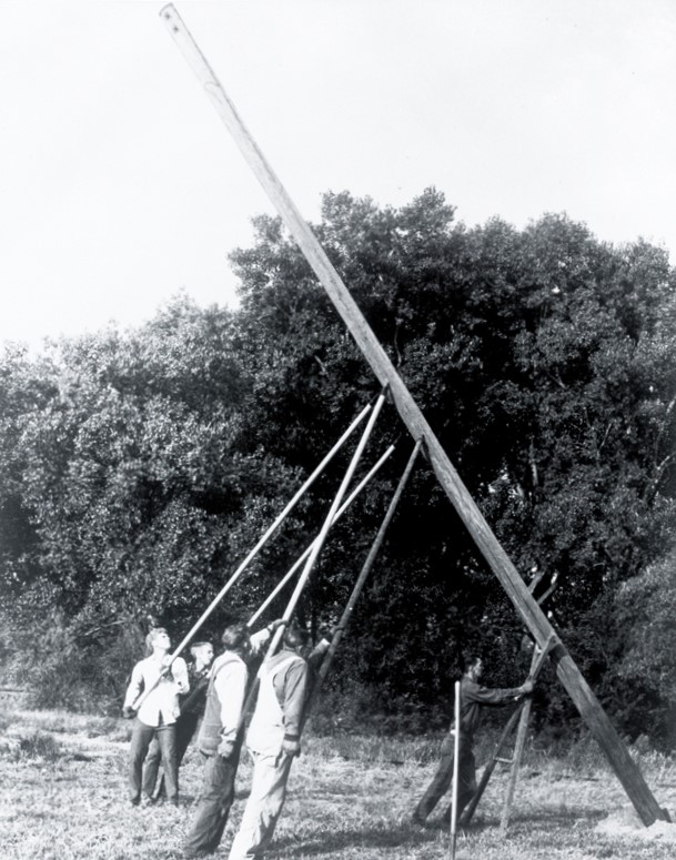 A group of five workers raising a utility pole by hand