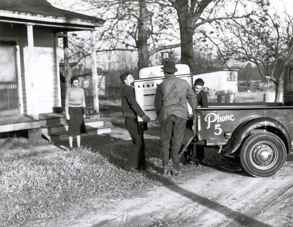 Three men unload a new stove for a rural woman. Source: The Next Greatest Thing, published by NRECA