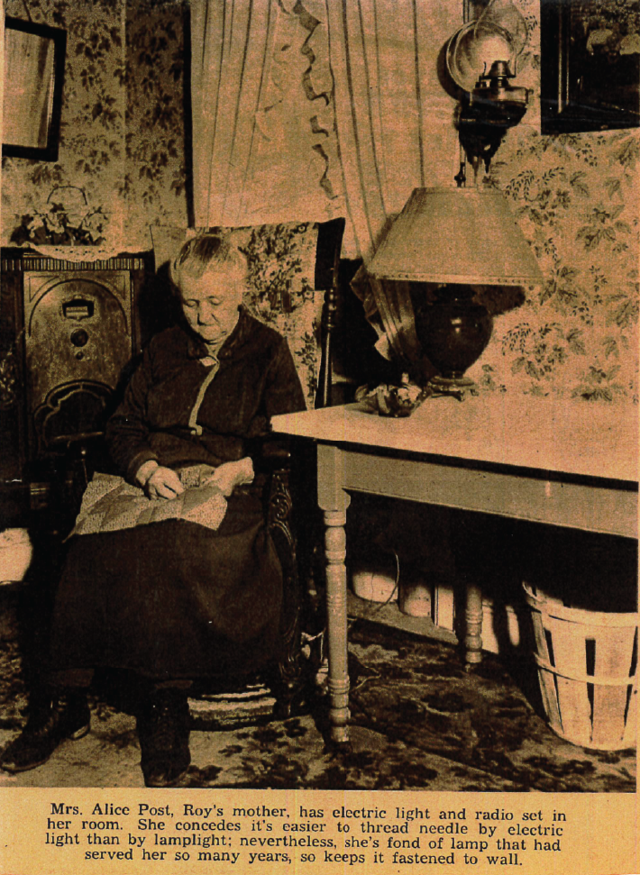 Photo of older woman, Alice Post, knitting by electric lamp light. An old lamp is mounted to the wall. From the Sussex Independent: “Mrs. Alice Post, Roy’s mother, has electric light and radio set in her room. She concedes it’s easier to thread needle by electric light than by lamplight; nevertheless, she’s fond of lamp that had served her so many years, so keeps it fastened to wall.”