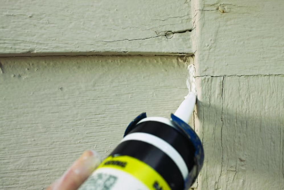 Closeup of someone using a caulk gun to seal cracks in their home's exterior