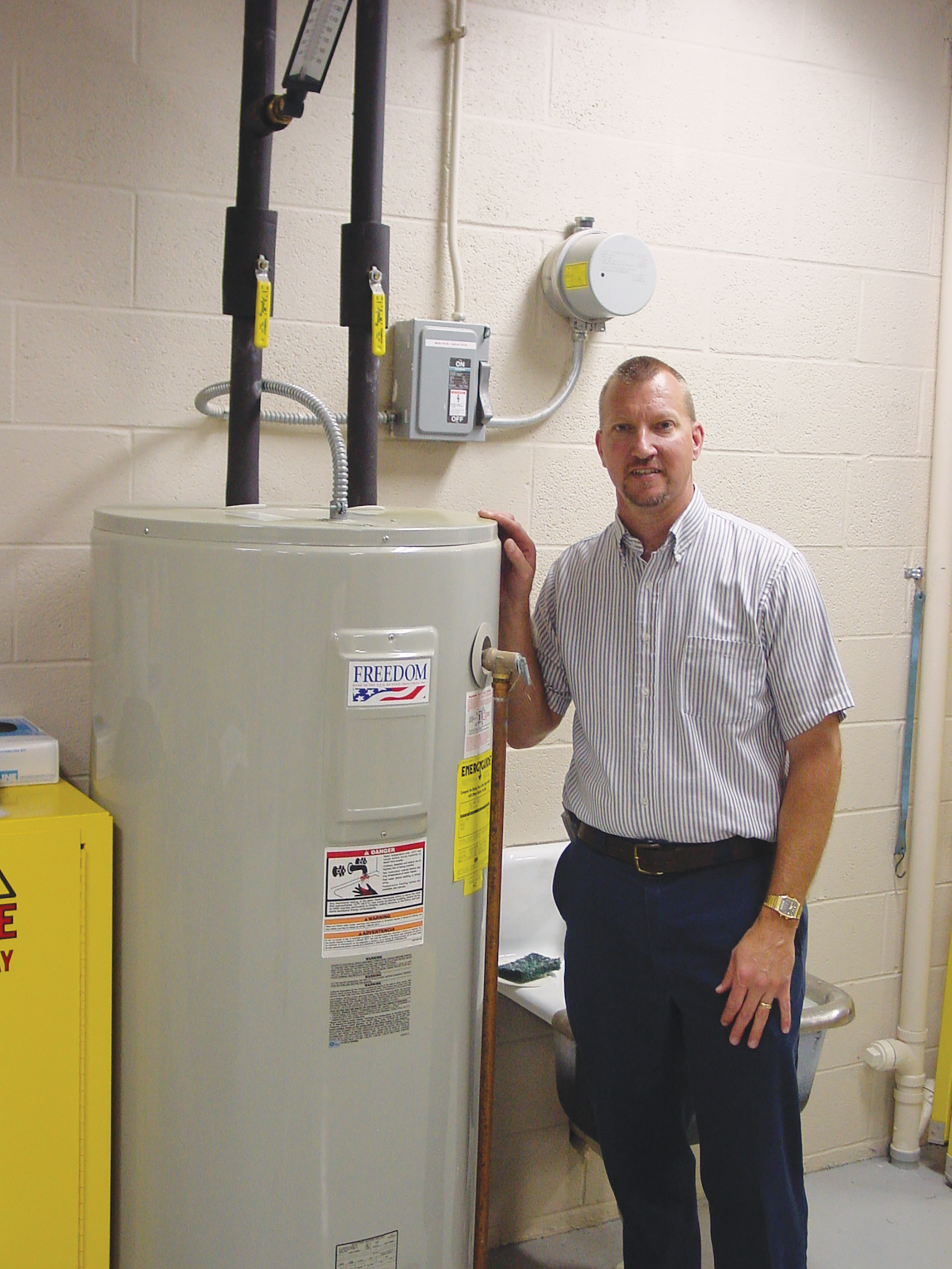 A SWITCH THAT SAVES: Brian Shearer, senior staff engineer at Gettysburg-based Adams Electric Cooperative, stands beside a water heater equipped with a load control receiver. When members volunteer to have these systems installed in their homes, it helps the cooperative manage purchased power costs and offer stable rates.