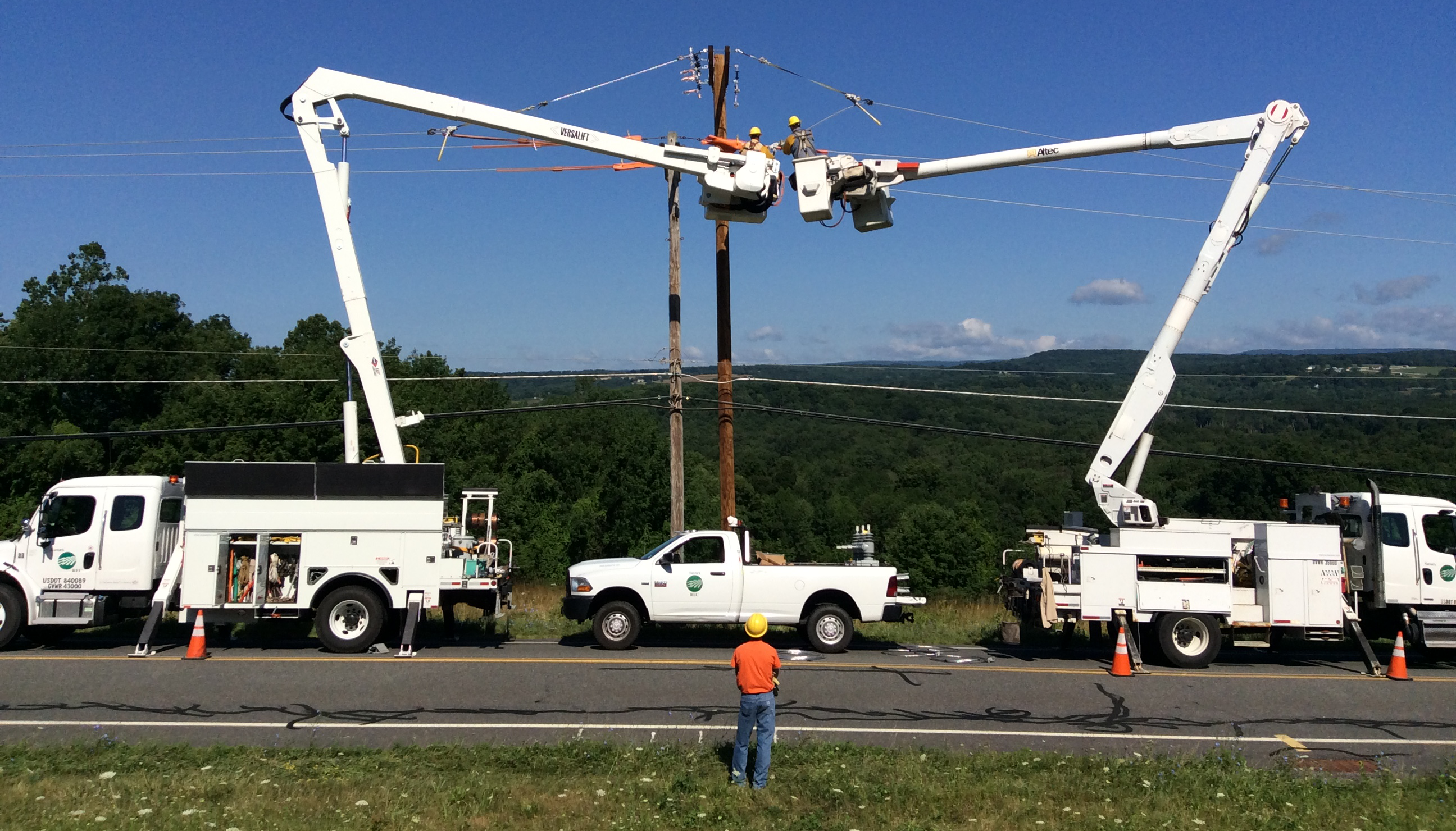 Lineworker observing from across the road as two other lineworkers in bucket trucks work on power lines.