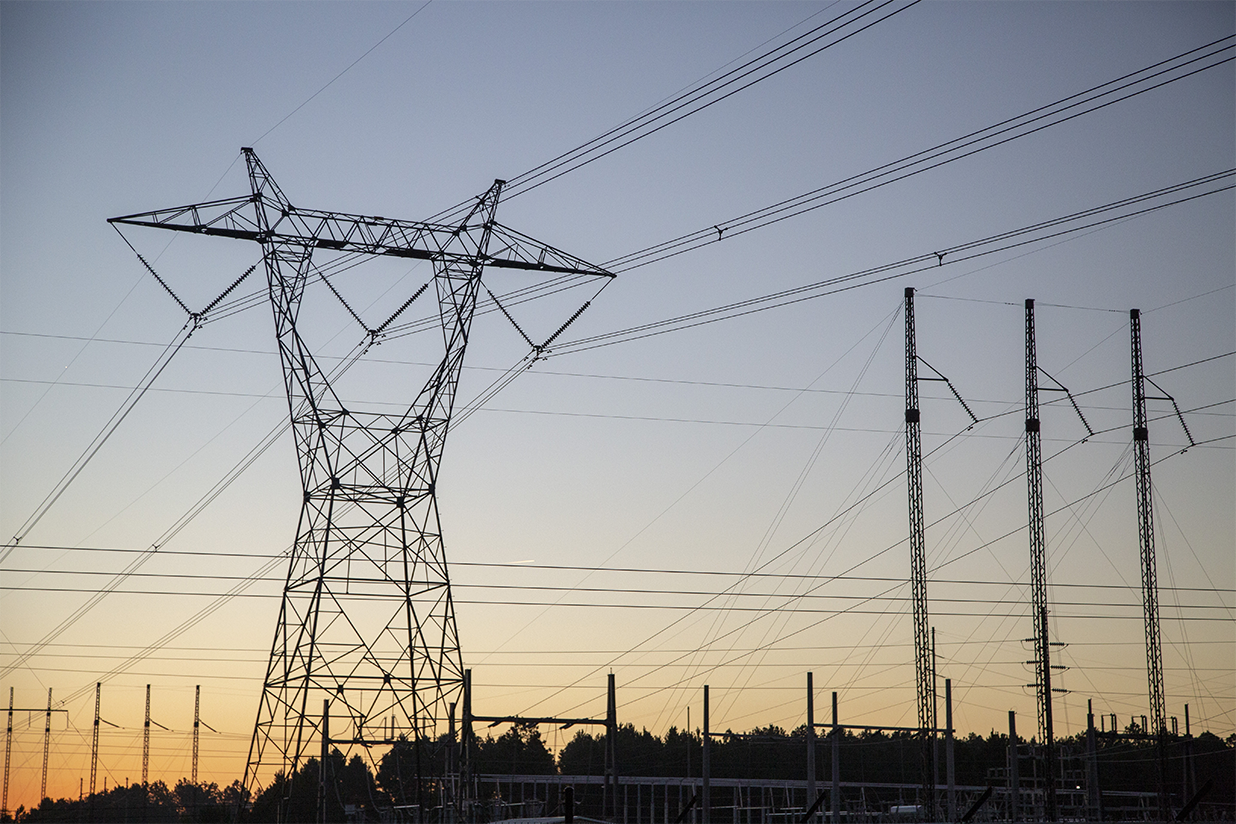 Photo of a transmission tower carrying high voltage transmission lines, silhouetted against the sunset
